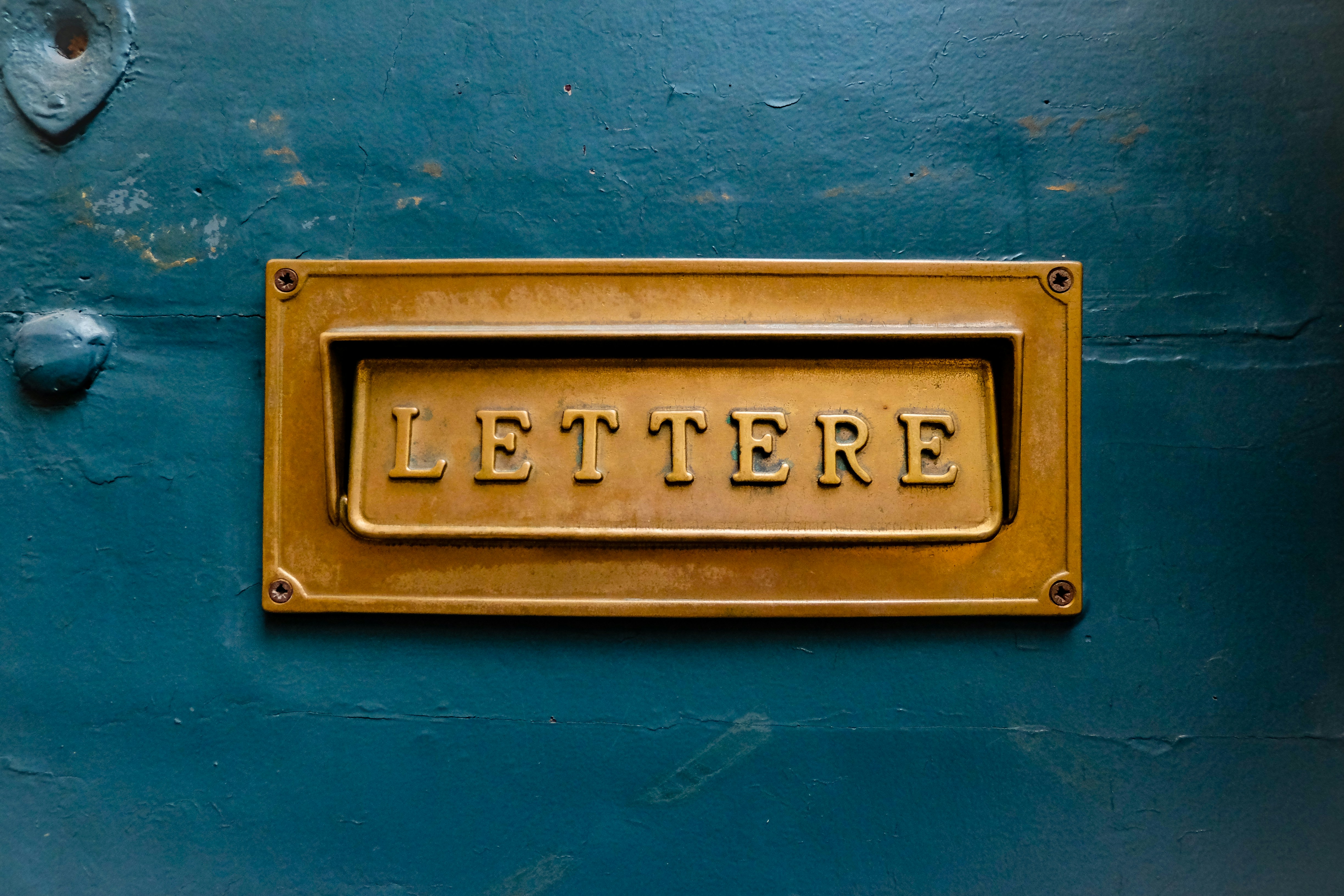 Brass letter slot reading LETTERE on a teal door